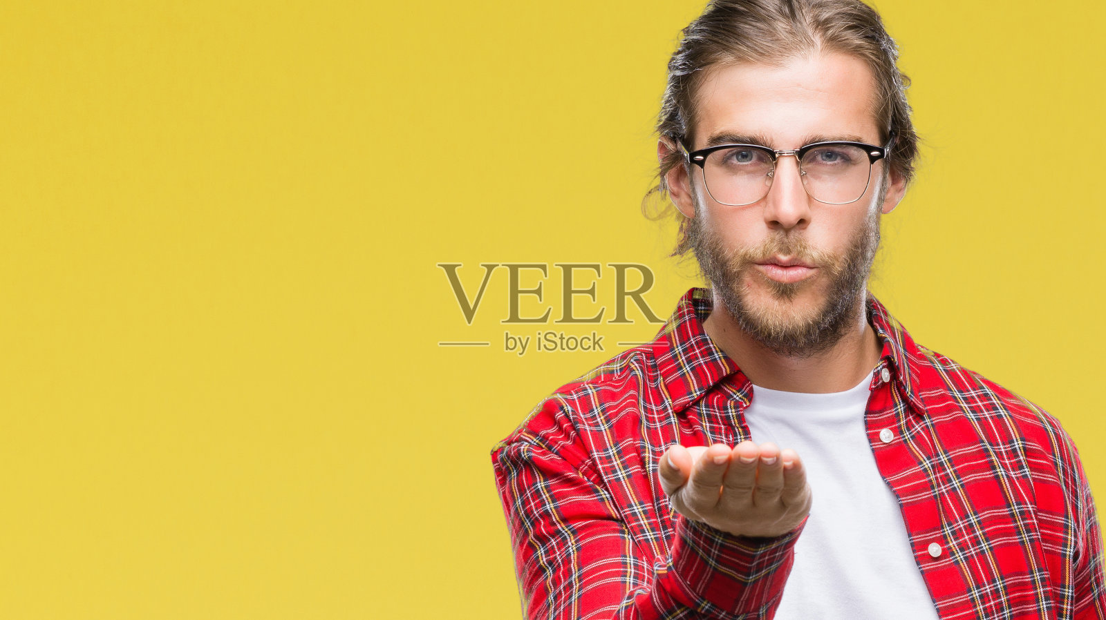 年轻英俊的长头发的男人戴眼镜在孤立的背景下看着镜头飞吻与手在空中是可爱和性感的。爱的表达。照片摄影图片