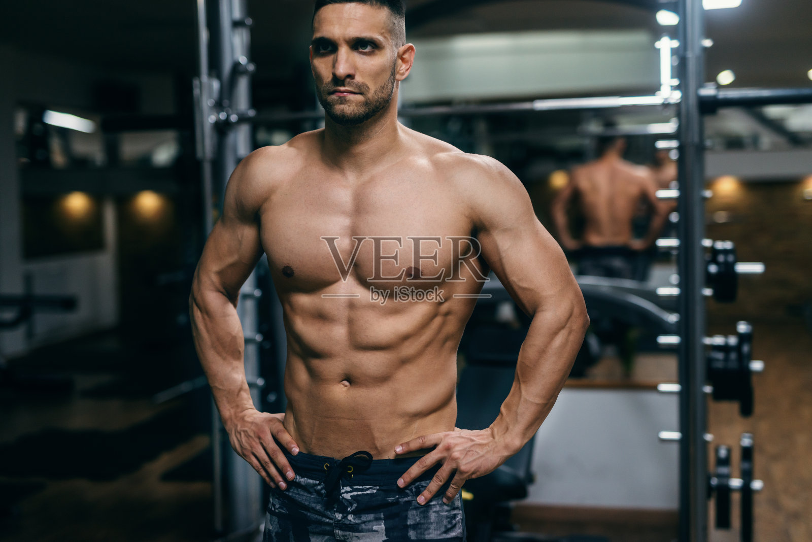 白人肌肉赤膊男子与手在臀部摆姿势在一个健身房。照片摄影图片