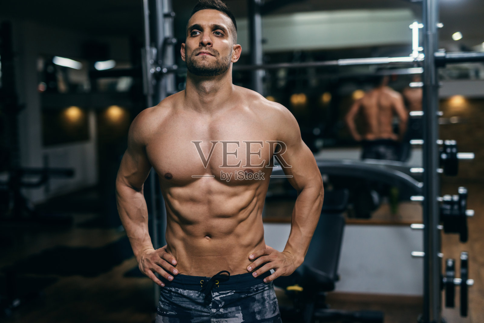 白人肌肉赤膊男子与手在臀部摆姿势在一个健身房。照片摄影图片