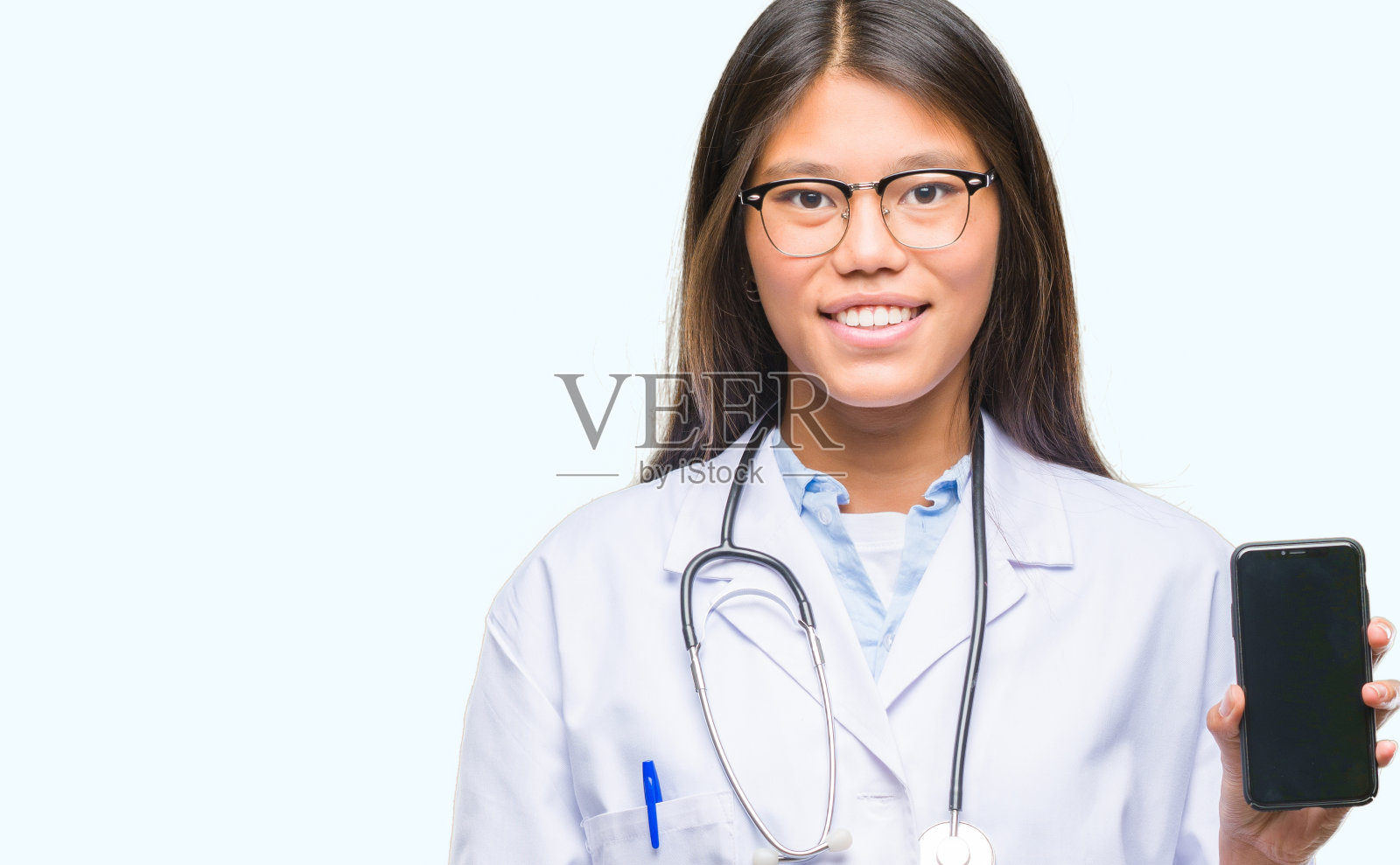 年轻的亚洲女医生拿着智能手机在孤立的背景下，一个快乐的脸站在那里，自信地微笑着露出牙齿照片摄影图片