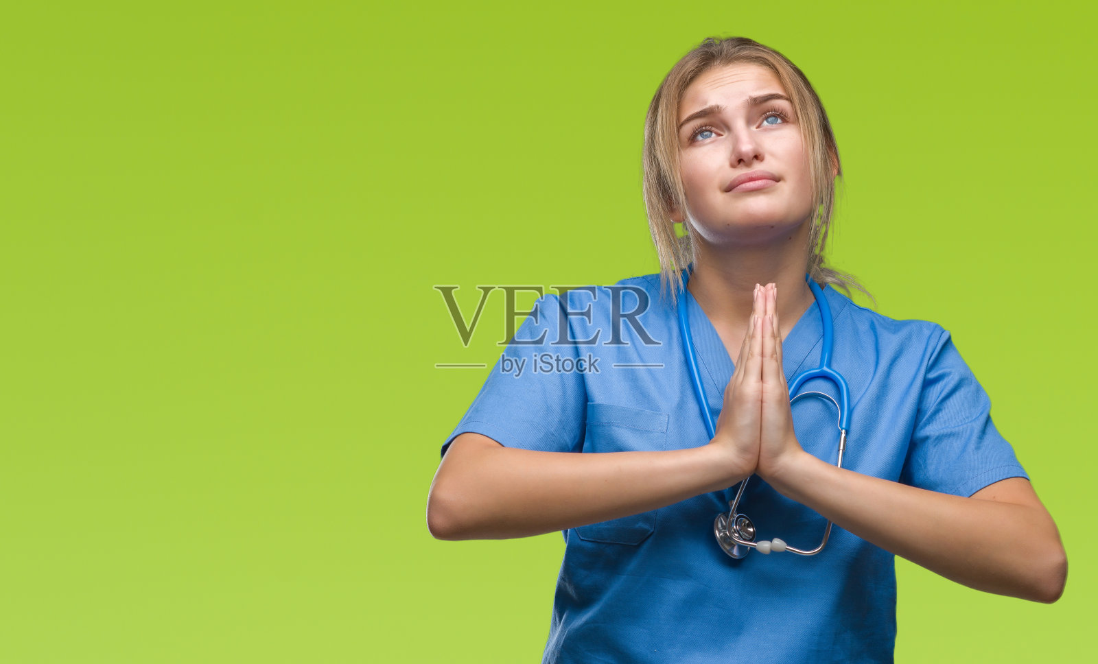 年轻的白种女医生穿着外科医生制服在孤立的背景乞求和祈祷与希望的表情在脸上非常情绪化和担心。请求宽恕。宗教的概念。照片摄影图片