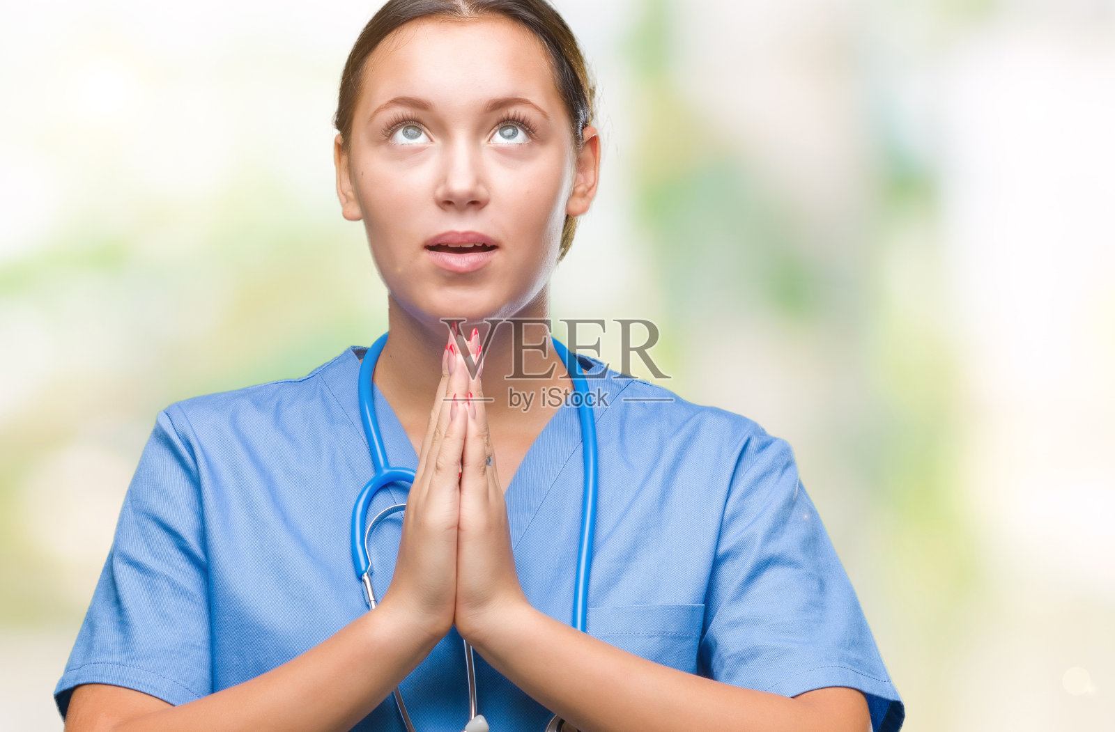 年轻的白种女医生穿着医疗制服在孤立的背景乞求和祈祷与希望的表情在脸上非常情绪化和担心。请求宽恕。宗教的概念。照片摄影图片