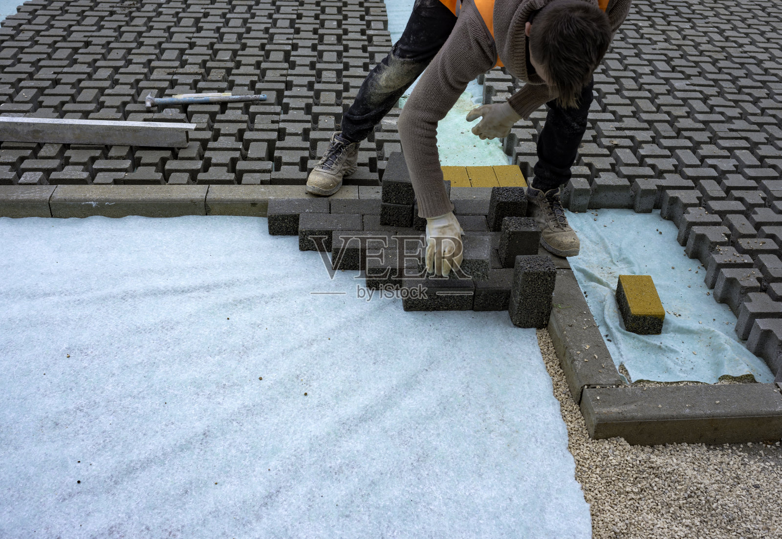 建筑工人在无纺布垫层上铺设联锁铺路混凝土并将其安装到位。照片摄影图片