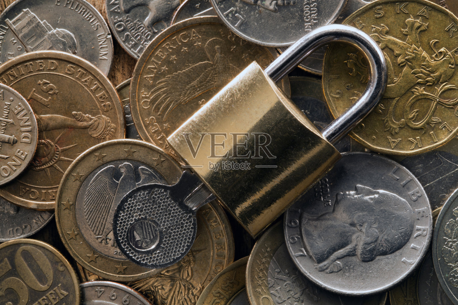 挂锁和钥匙躺在一堆各种各样的硬币上照片摄影图片