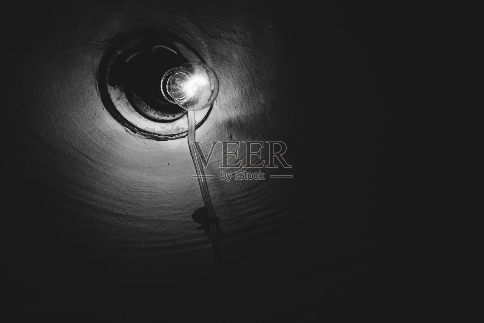 白炽灯在暗室里燃烧特写。照明。粗糙墙上的旧灯泡。地下室的灯光呈灰度。光在黑暗中。极简主义的单色背景。副本的空间。照片摄影图片