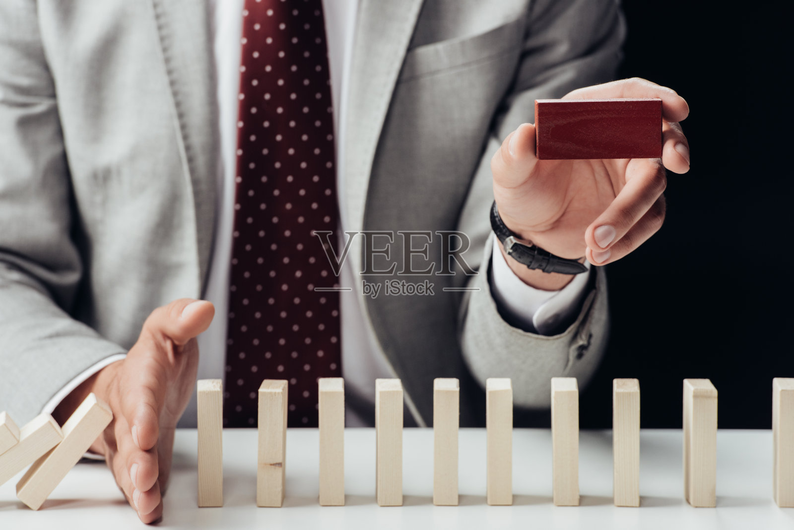 穿着西装的商人抱着红砖，防止木块落在黑色上照片摄影图片