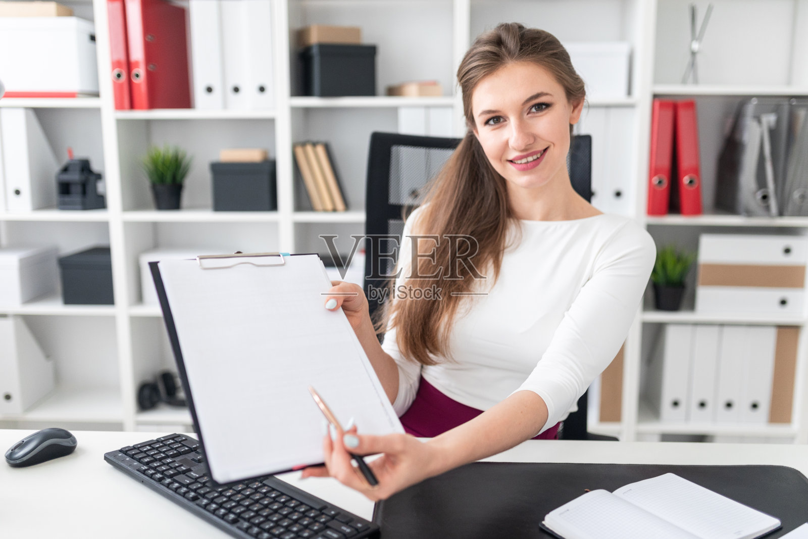 一个年轻女孩坐在桌子旁，拿出一张白纸上的一支笔。照片摄影图片