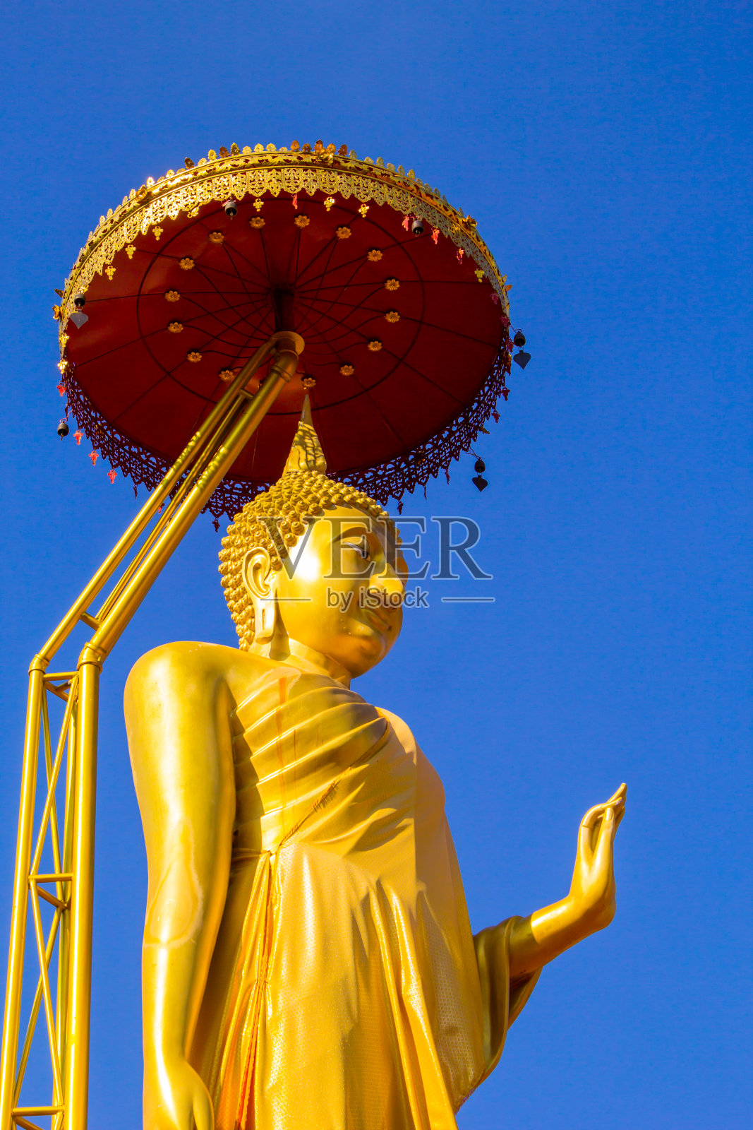 金佛站在金色的伞与清澈的蓝天背景。照片摄影图片