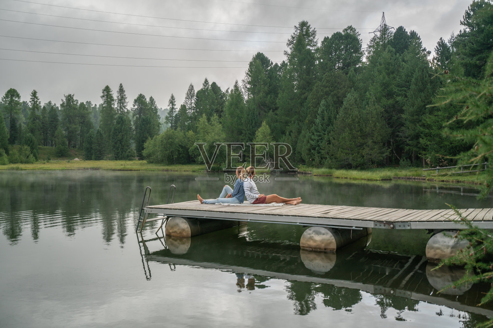 年轻夫妇在阴天里的湖边码头上放松身心，享受大自然和绿色环境照片摄影图片