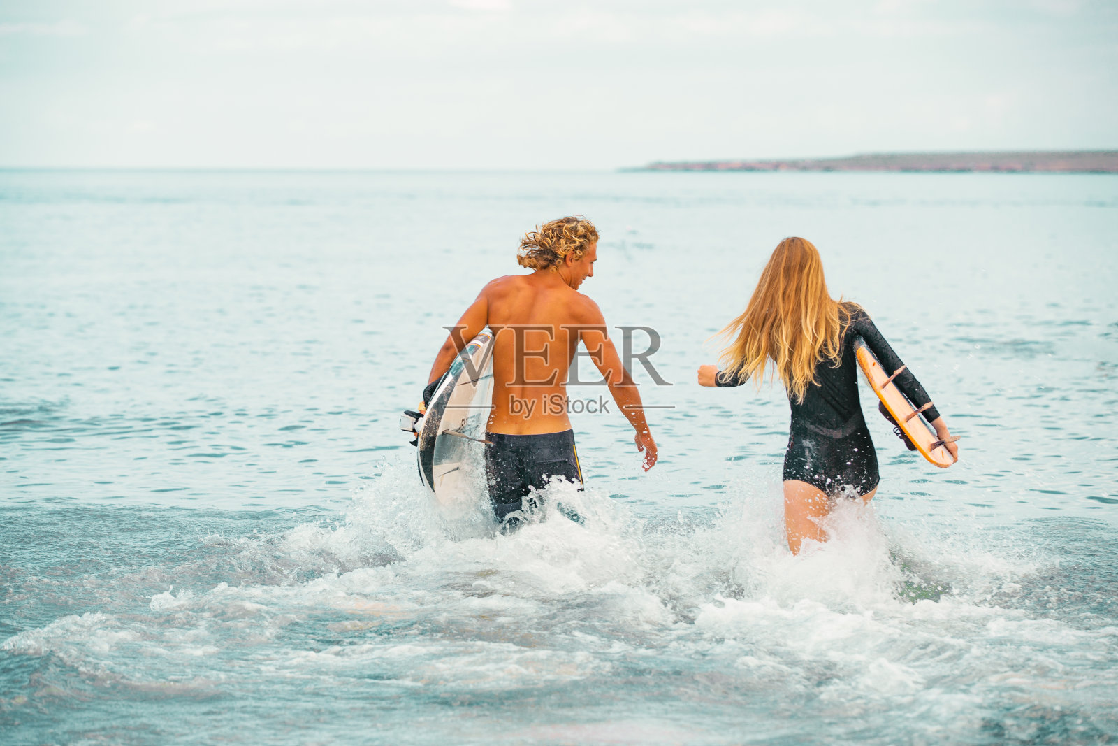 在海滩冲浪者-微笑的一对冲浪者在海滩上散步，在夏天有乐趣。极限运动和度假概念照片摄影图片