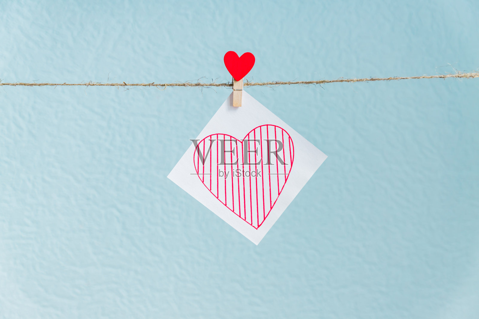 红色情人节爱心别针挂在天然绳上，以蓝色为底色。画在纸上的心。照片摄影图片