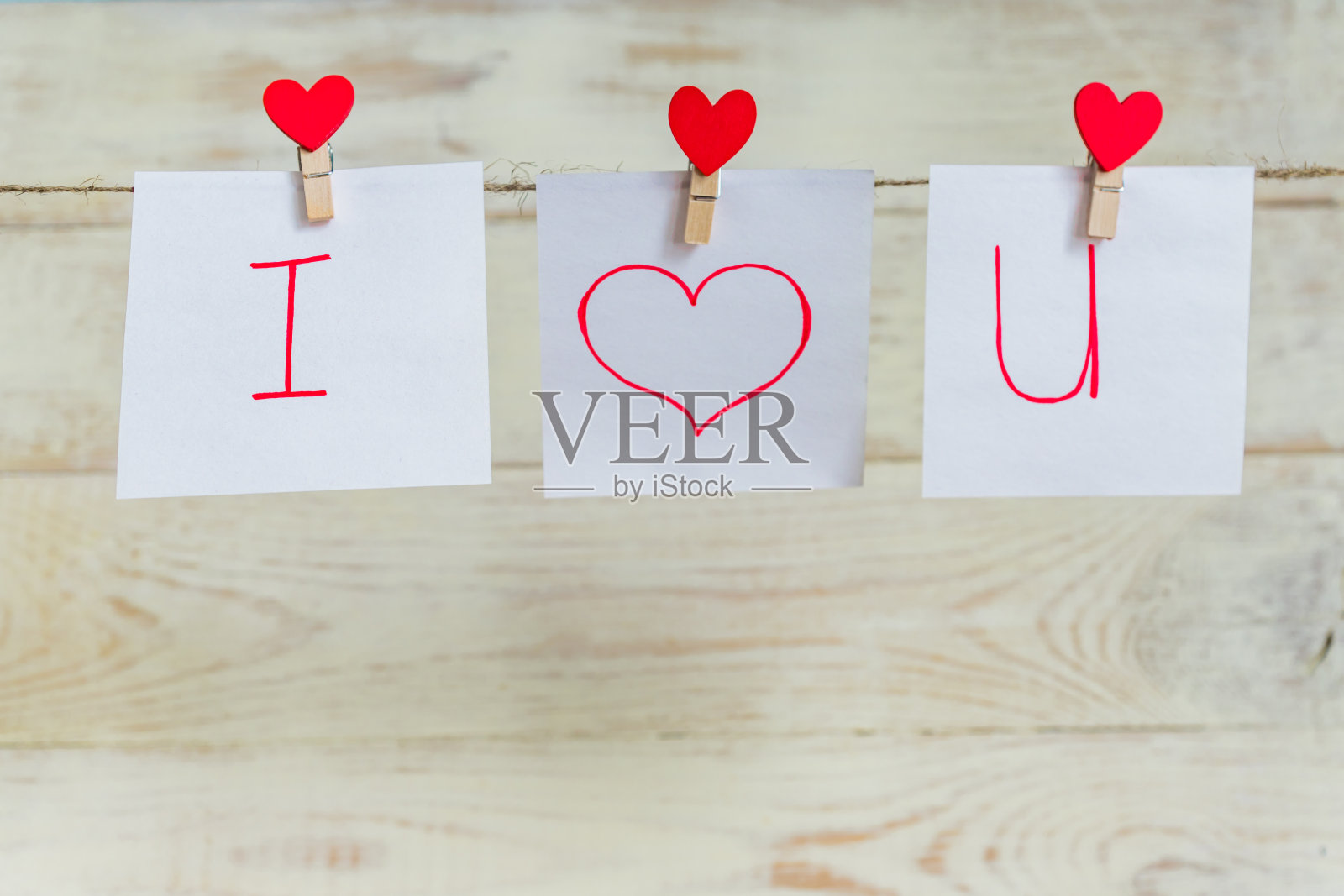 白色的木质背景下，红色的情人节心形别针挂在天然的绳子上。我爱你铭文在纸上。照片摄影图片