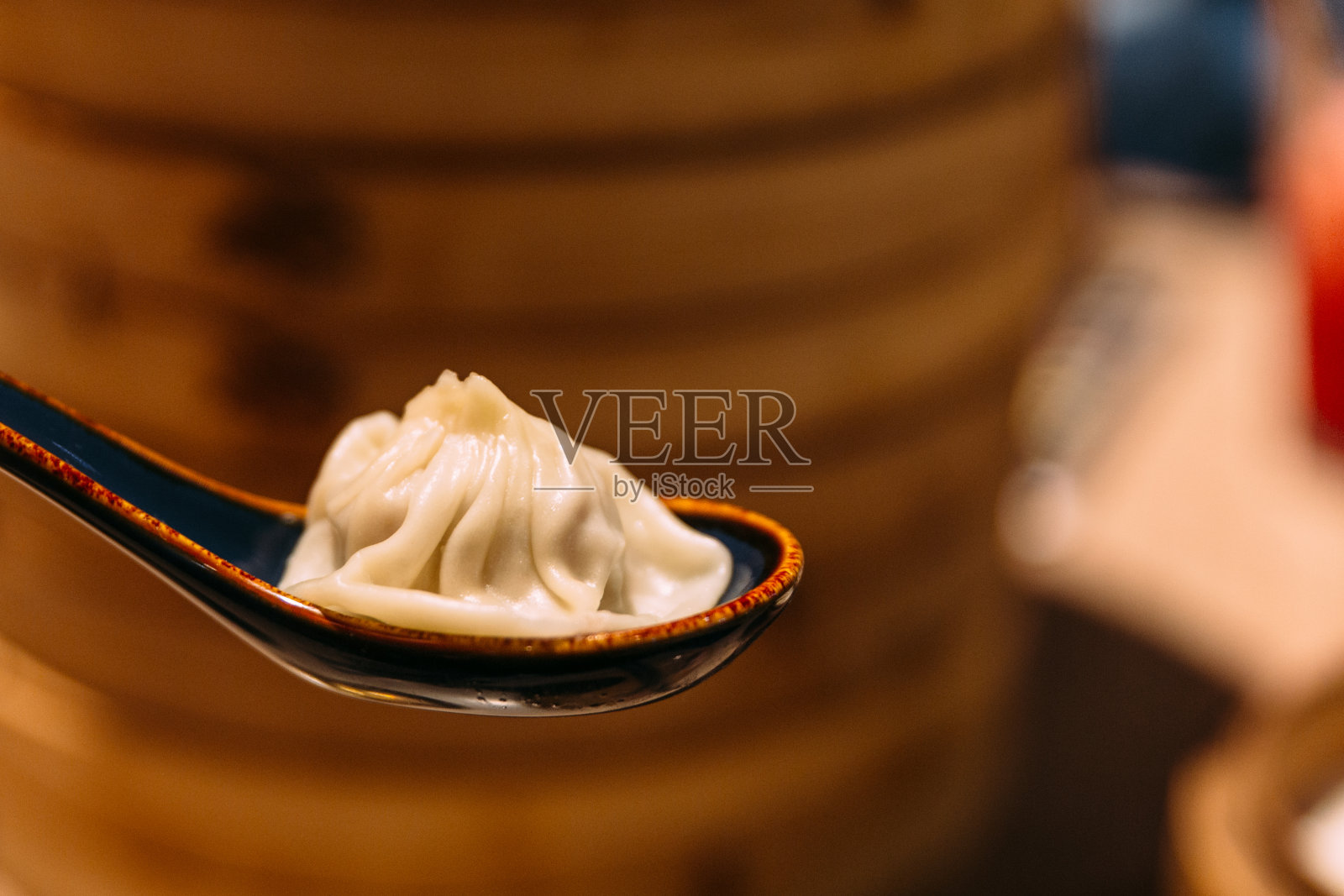 小笼包在勺子和模糊的竹篓在背景。照片摄影图片