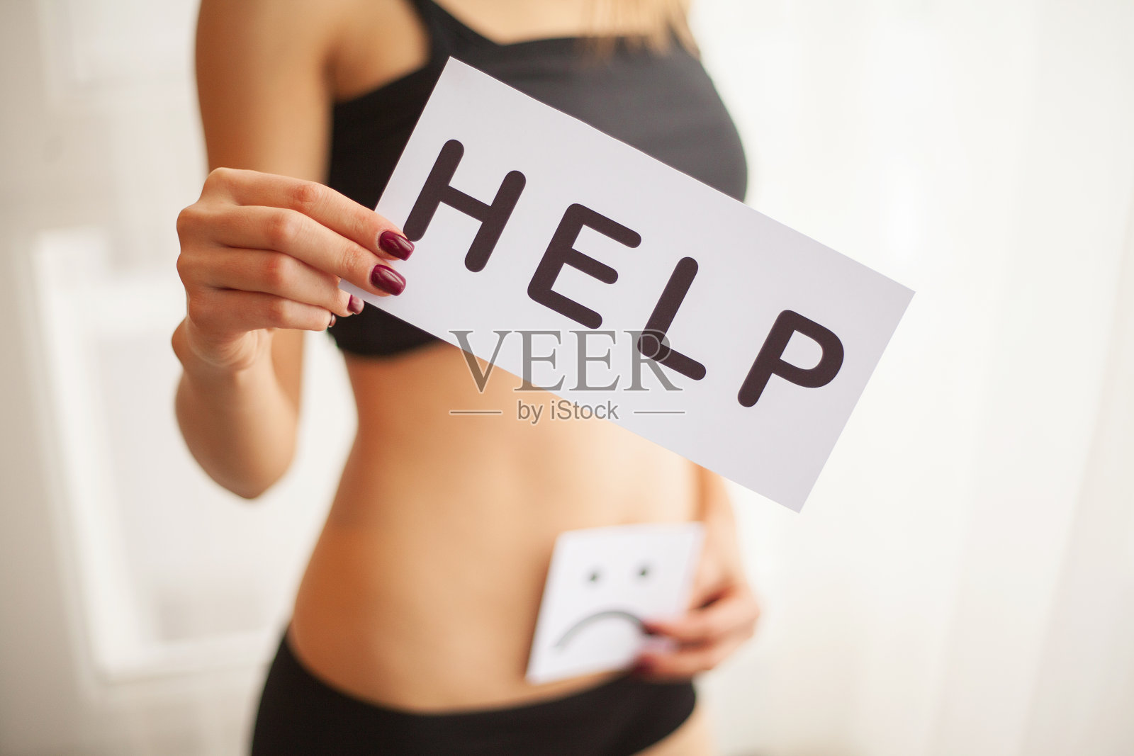 女人的健康问题。女性与Fit苗条的身体在内裤拿着白色卡片与词帮助靠近她的肚子的特写。消化紊乱，经期疼痛，健康问题概念。高分辨率照片摄影图片