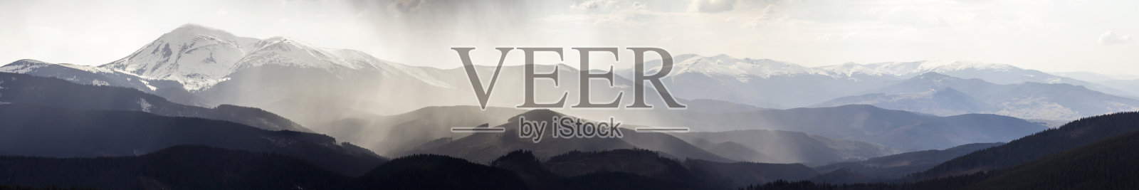 壮丽的喀尔巴阡山脉壮丽的全景，覆盖着常青的森林在薄雾宁静的早晨或晚上在黑暗多云的天空。远处的山顶上覆盖着积雪。照片摄影图片