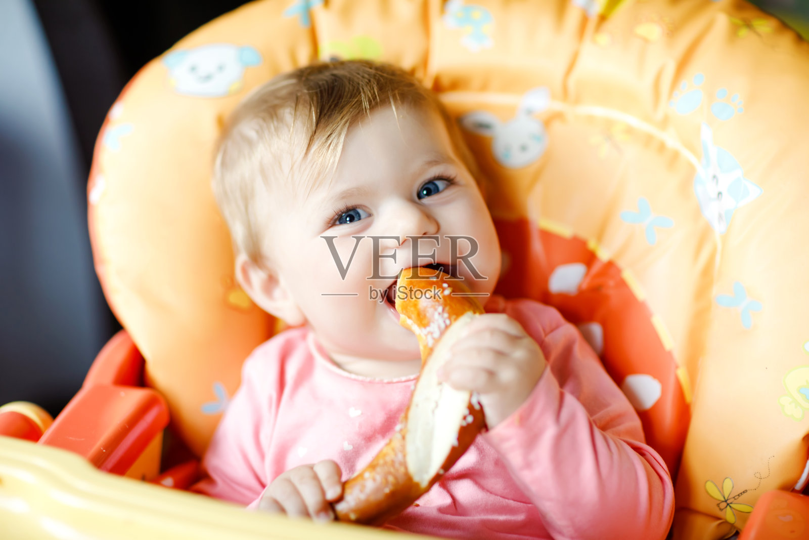 可爱的小女孩在吃面包。孩子第一次吃一片椒盐卷饼。母乳喂养后的第一餐。健康宝宝玩得开心。照片摄影图片