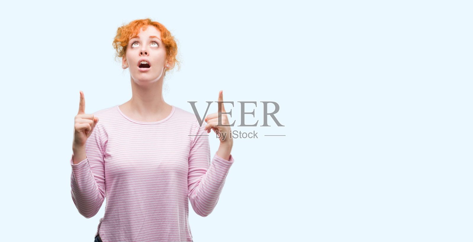 年轻的红发女子惊讶地抬起头，用手指着手指着。照片摄影图片