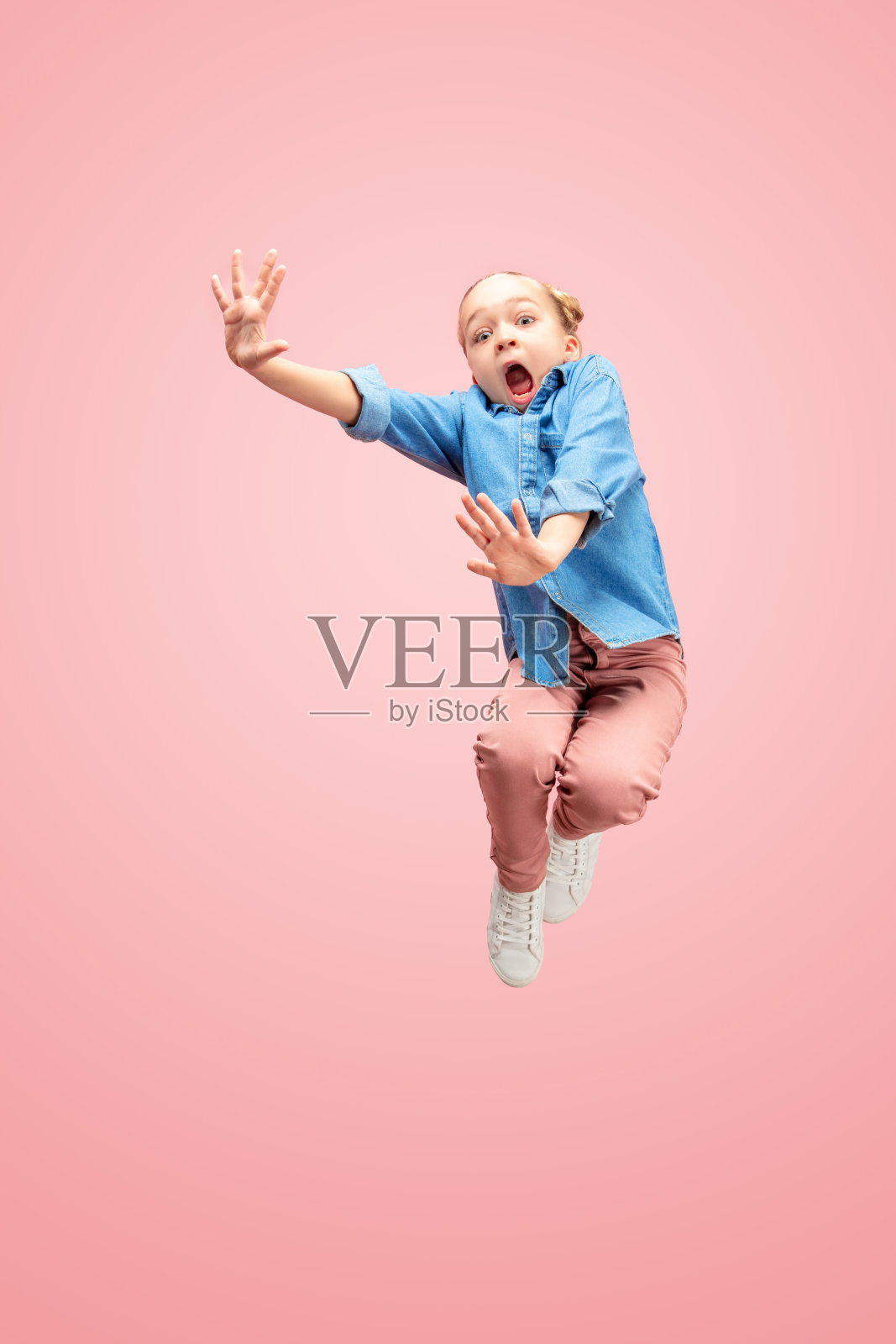 年轻害怕的白人少女在空中跳，孤立在粉红色的工作室背景。照片摄影图片