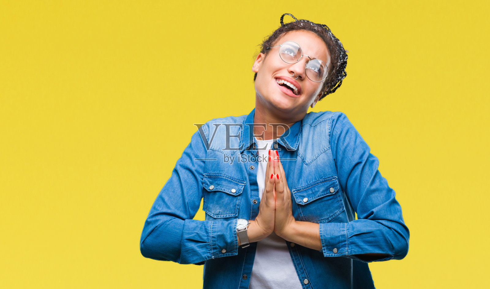 年轻的梳着辫子戴着眼镜的非洲裔美国女孩在孤立的背景下乞讨和祈祷，双手在一起，脸上带着希望的表情非常情绪化和担心。请求宽恕。宗教的概念。照片摄影图片