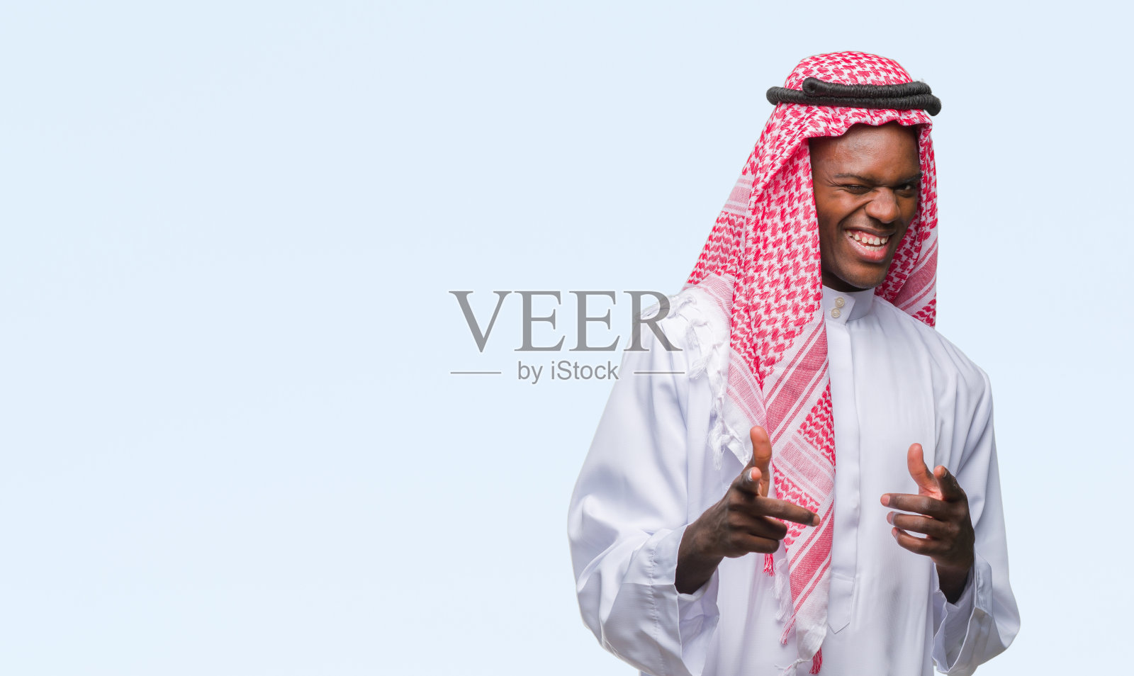 年轻的阿拉伯裔非洲人穿着传统的keffiyeh在孤立的背景指向手指与快乐和有趣的脸相机。良好的能量和共鸣。照片摄影图片