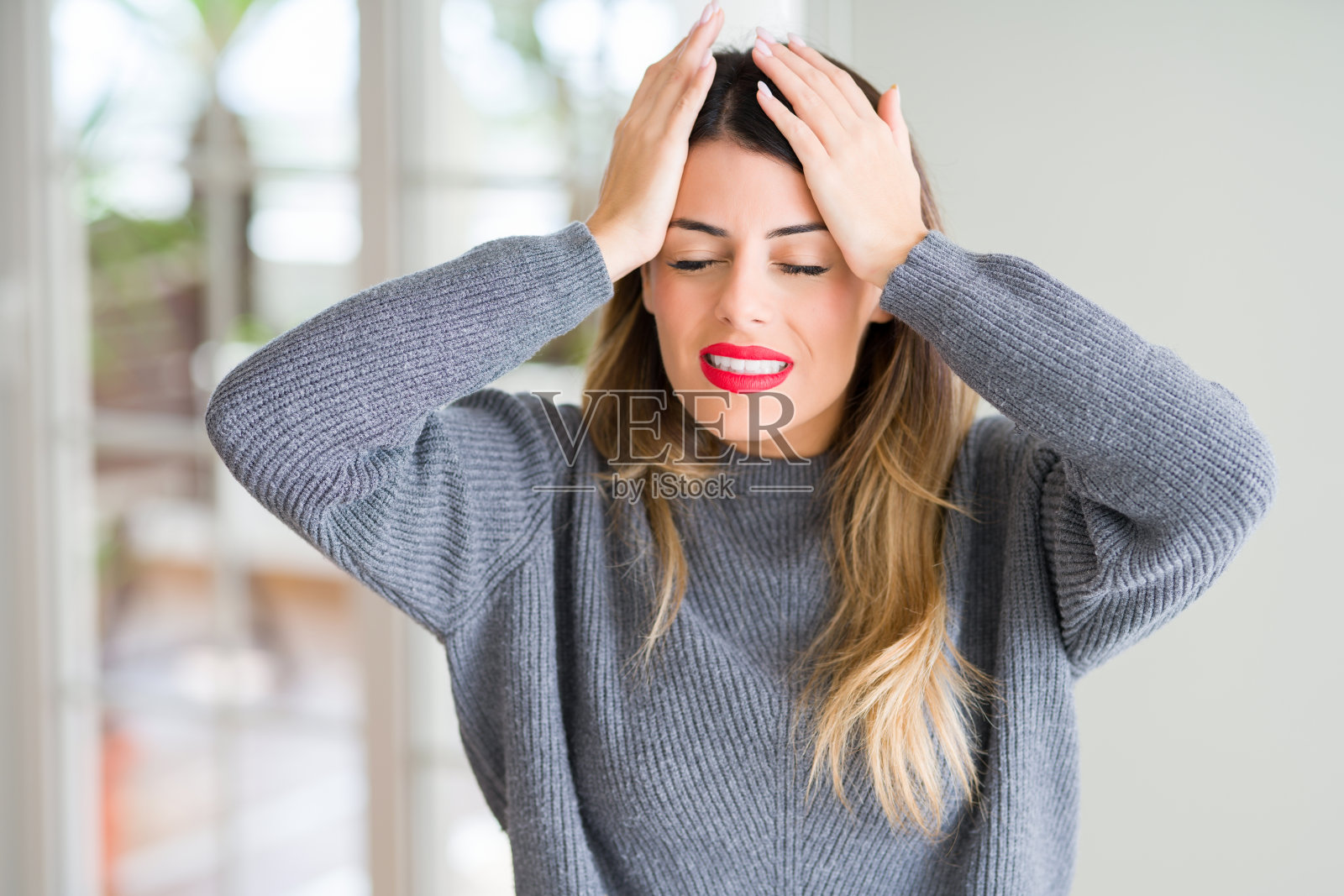 年轻漂亮的居家女子身穿冬季毛衣，头痛欲裂，双手抱头照片摄影图片