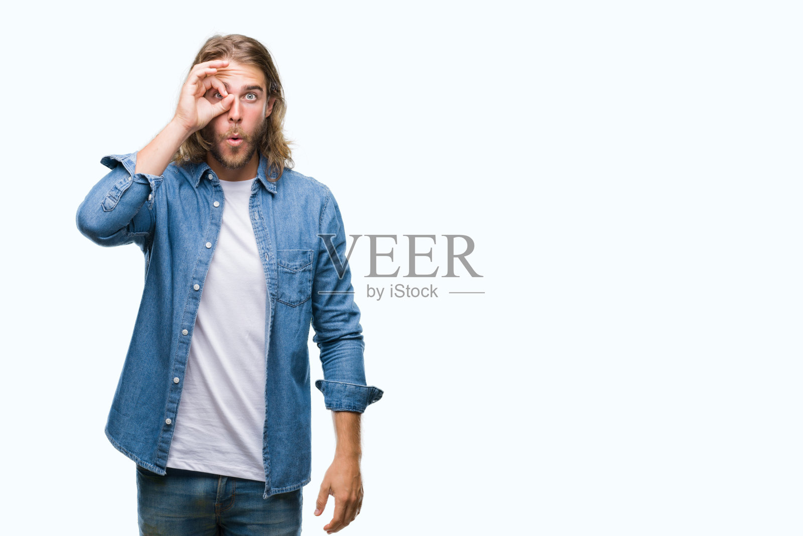 年轻英俊的男子与长头发在孤立的背景做ok手势震惊与惊讶的脸，眼睛透过手指。不相信的表情。照片摄影图片