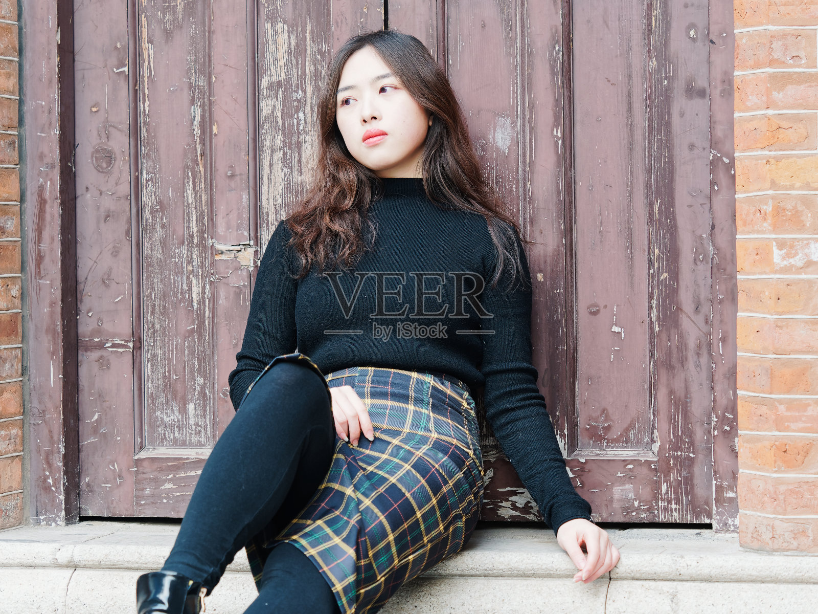 年轻漂亮的黑发女子穿着黑衣服坐在木门前的台阶上摆好姿势，等着有人回家。情感、人、美、生活理念。照片摄影图片