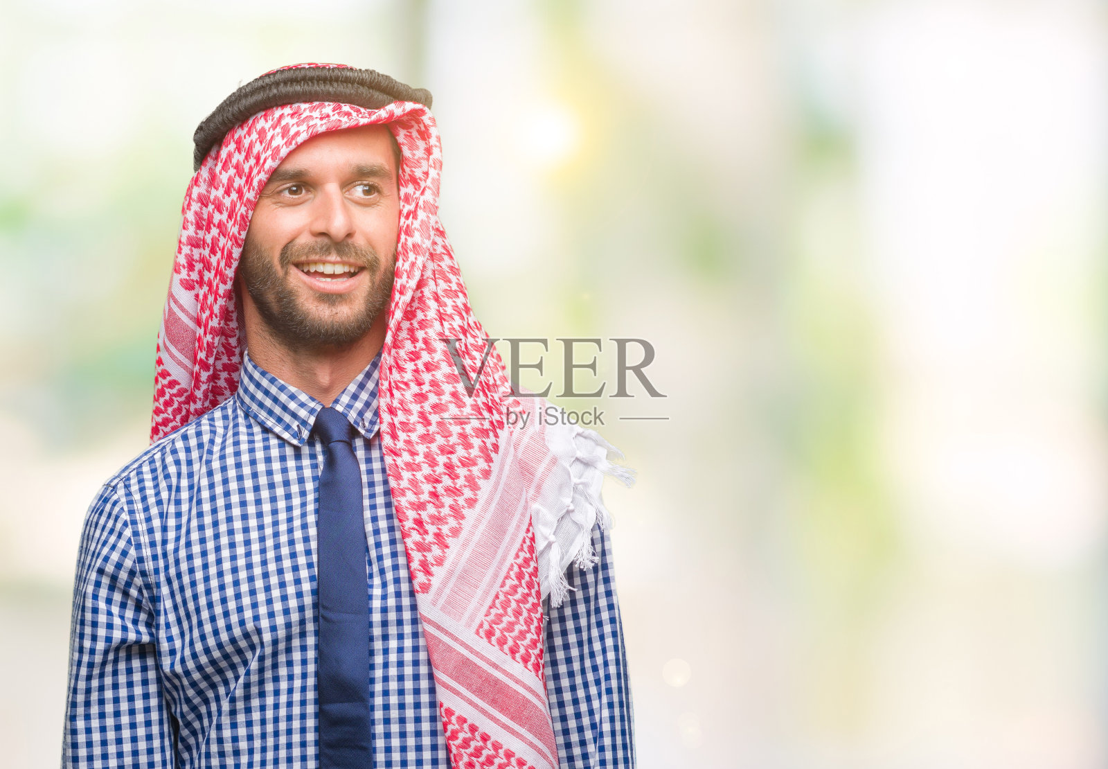 年轻英俊的阿拉伯商人穿着keffiyeh在孤立的背景看向一边，脸上微笑，自然的表情。自信的笑。照片摄影图片