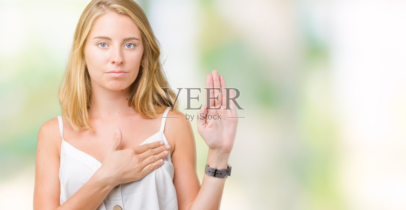 美丽的年轻女子在孤立的背景下发誓，手放在胸前，张开手掌，做出忠诚承诺的誓言照片摄影图片
