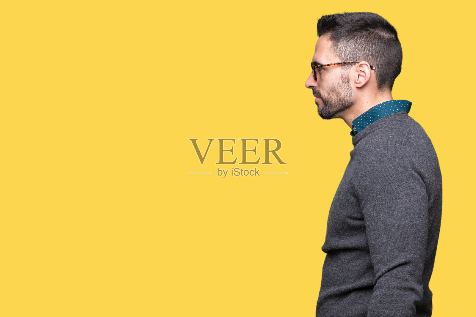 年轻英俊的男子戴着眼镜在孤立的背景看向一边，放松的侧面姿势与自然的脸与自信的微笑。照片摄影图片