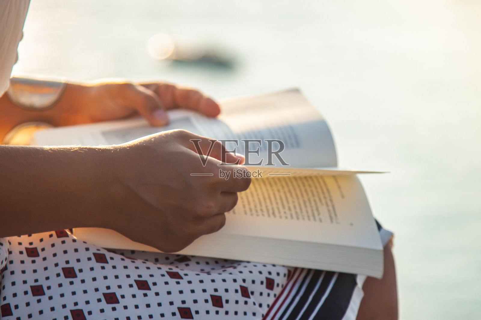 年轻的女子在海边阅读日落在庞扎岛海岸，坐在一堵墙与海洋的观点。照片摄影图片