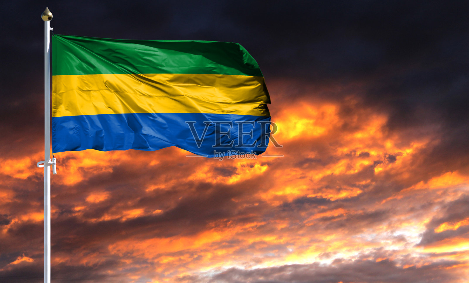 旗杆上的加蓬国旗迎风飘扬，映衬着五彩缤纷的晚霞天空照片摄影图片