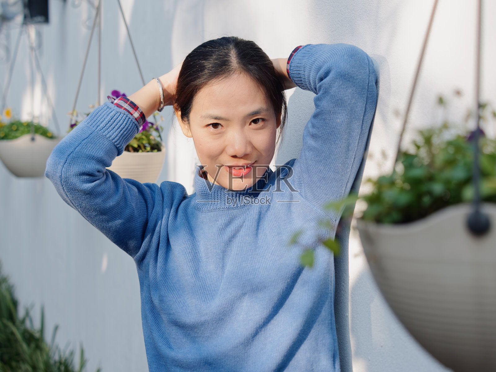 美丽的年轻的黑发女人在蓝色毛衣看着和微笑在院子里。户外时尚写真魅力中国商务时尚淑女。情感、家庭主妇、人、美、生活理念。照片摄影图片