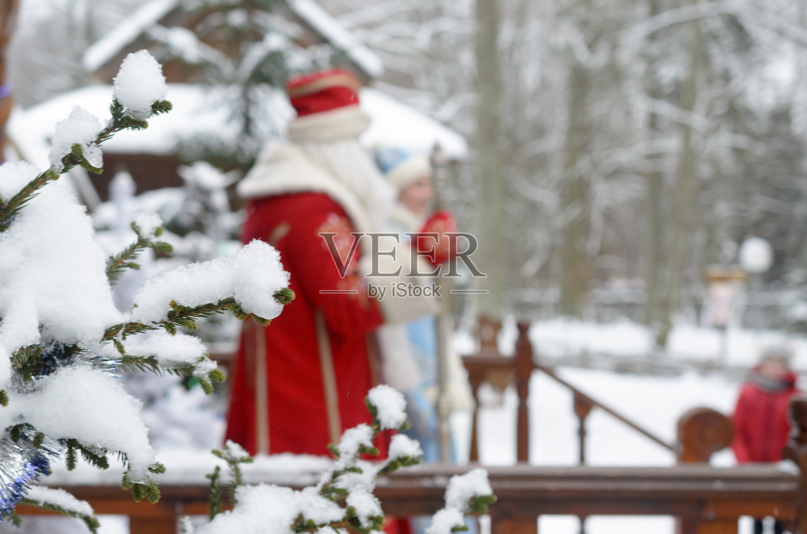 圣诞老人和雪姑娘在冬天走到他们庄园的露台上，背景是白雪覆盖的冷杉树。照片摄影图片