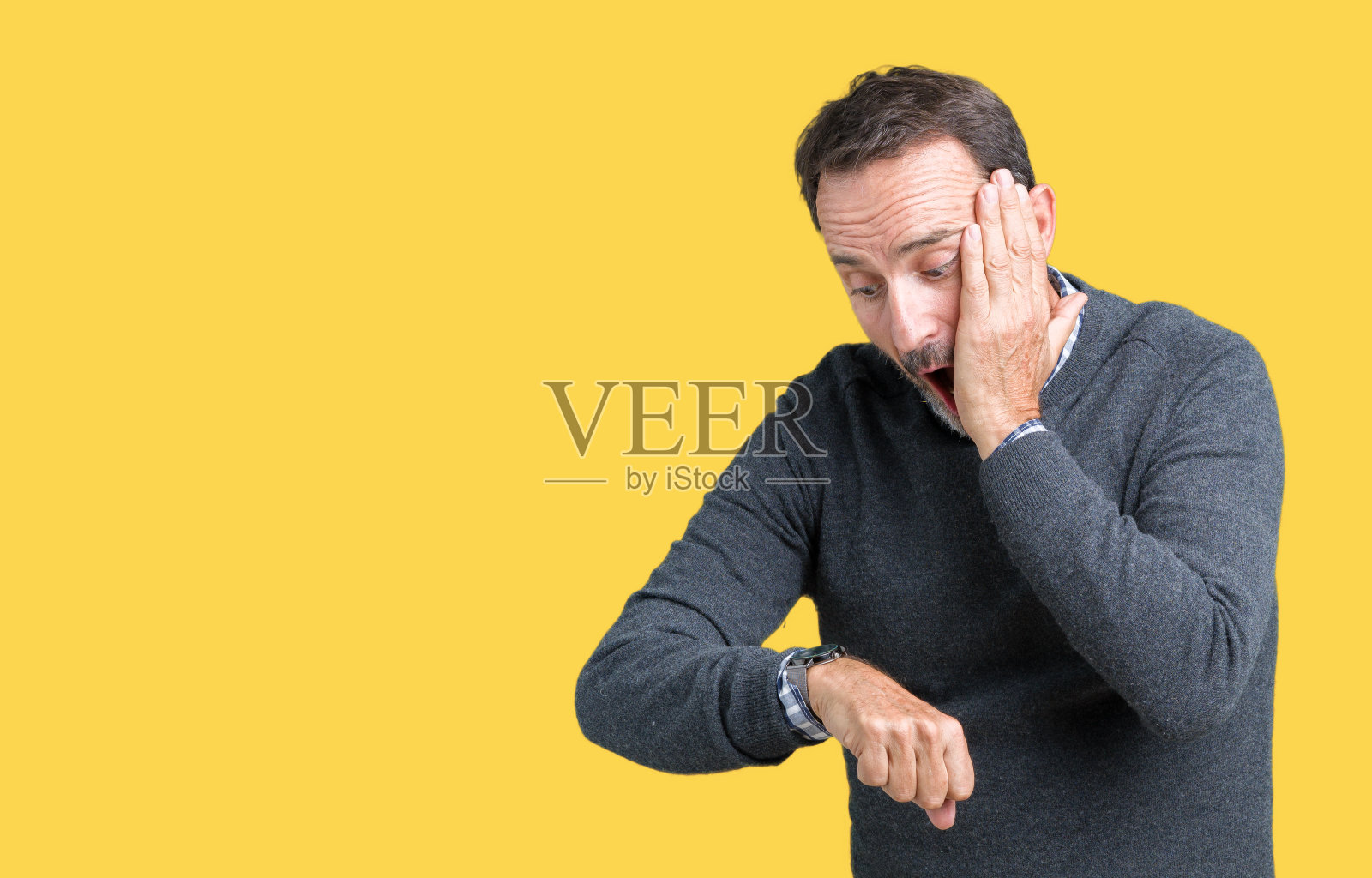 英俊的中年老人穿着毛衣越过孤立的背景看着手表着急的时间，害怕迟到照片摄影图片