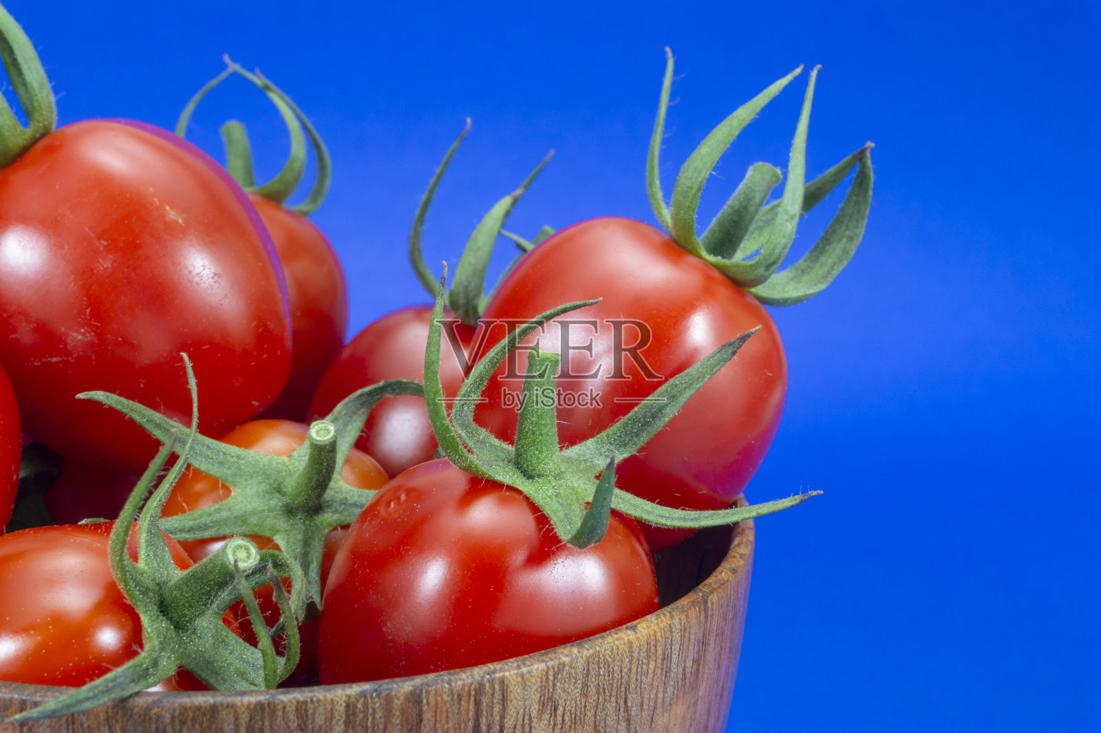 红色的圣女果在木碗里，上面是蓝色的照片摄影图片