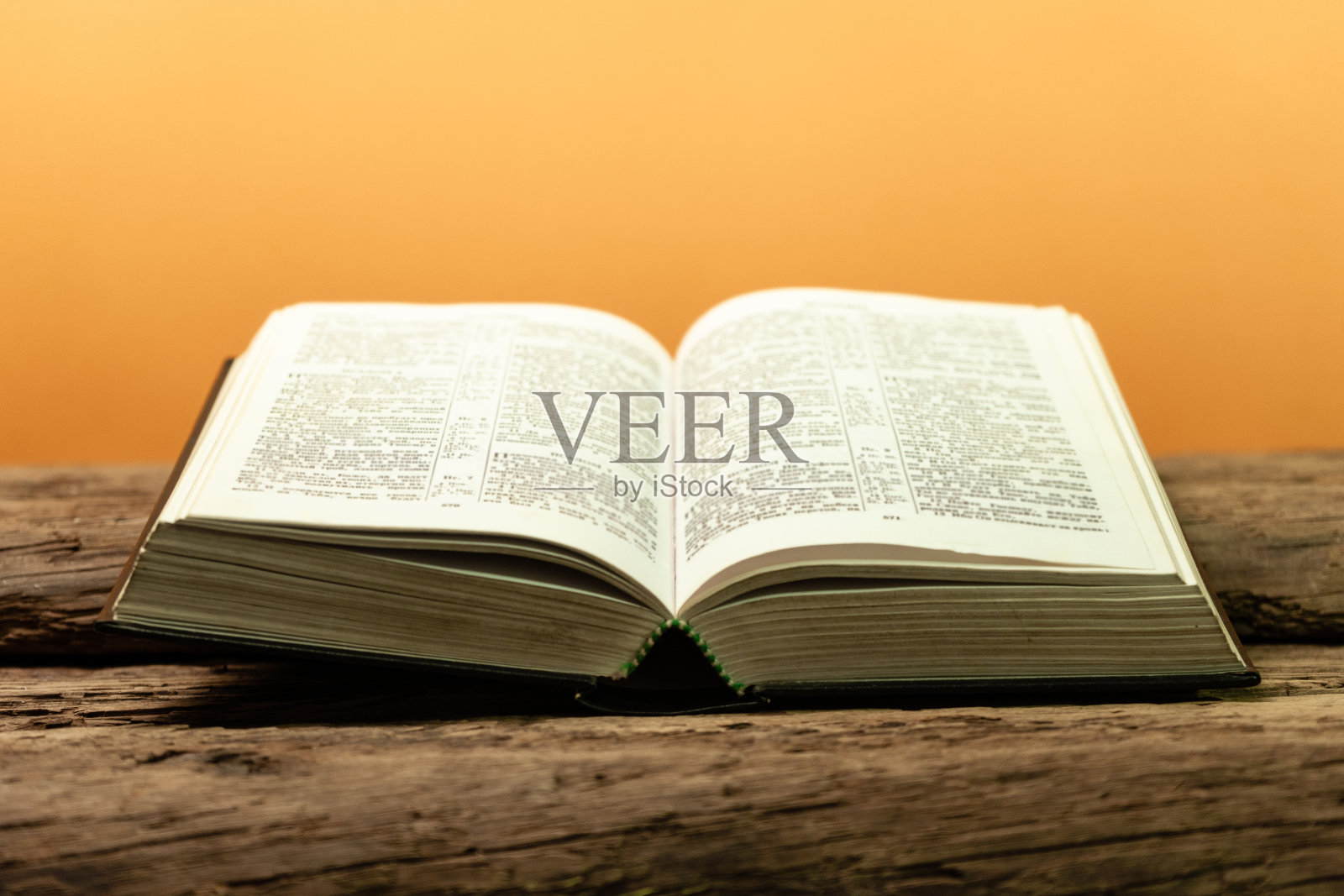 在旧橡木木桌上打开《圣经》。美丽的橙色背景。照片摄影图片