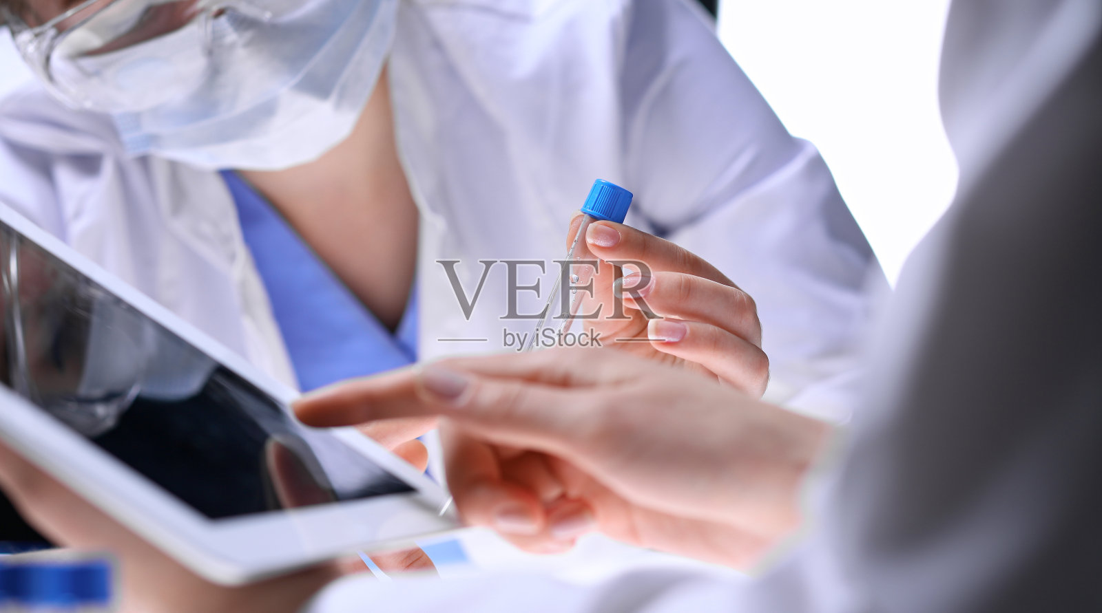 科学研究团队的特写，清晰的解决方案在实验室。金发女化学家拿着试管的玻璃，而她的同事用平板电脑检查结果。血液测试，医药或化学制造概念。照片摄影图片
