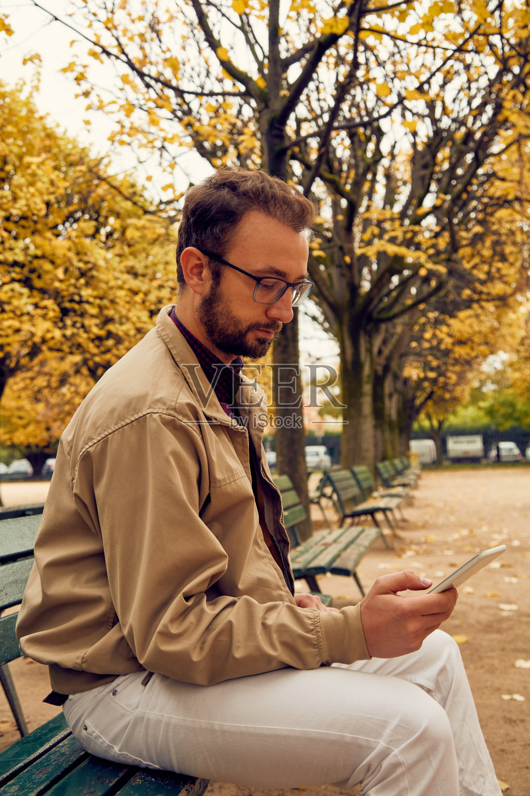 在欧洲的城市里，现代人坐在长椅上使用手机。照片摄影图片