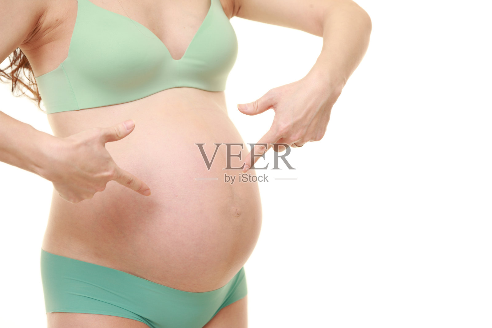 穿着绿色内衣的孕妇指着她的肚子照片摄影图片