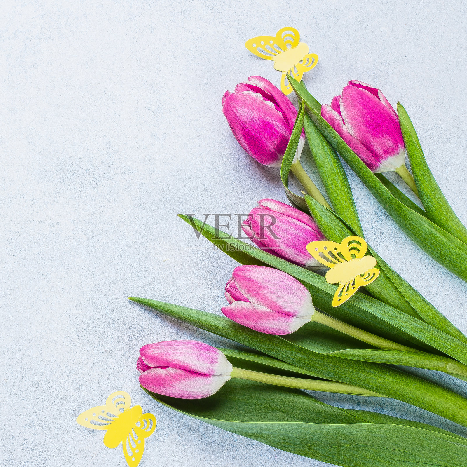 春天的粉红色郁金香和黄色纸蝴蝶在蓝色的石头背景为母亲节，3月8日。复活节假期的概念。俯视图，平放，复制空间照片摄影图片