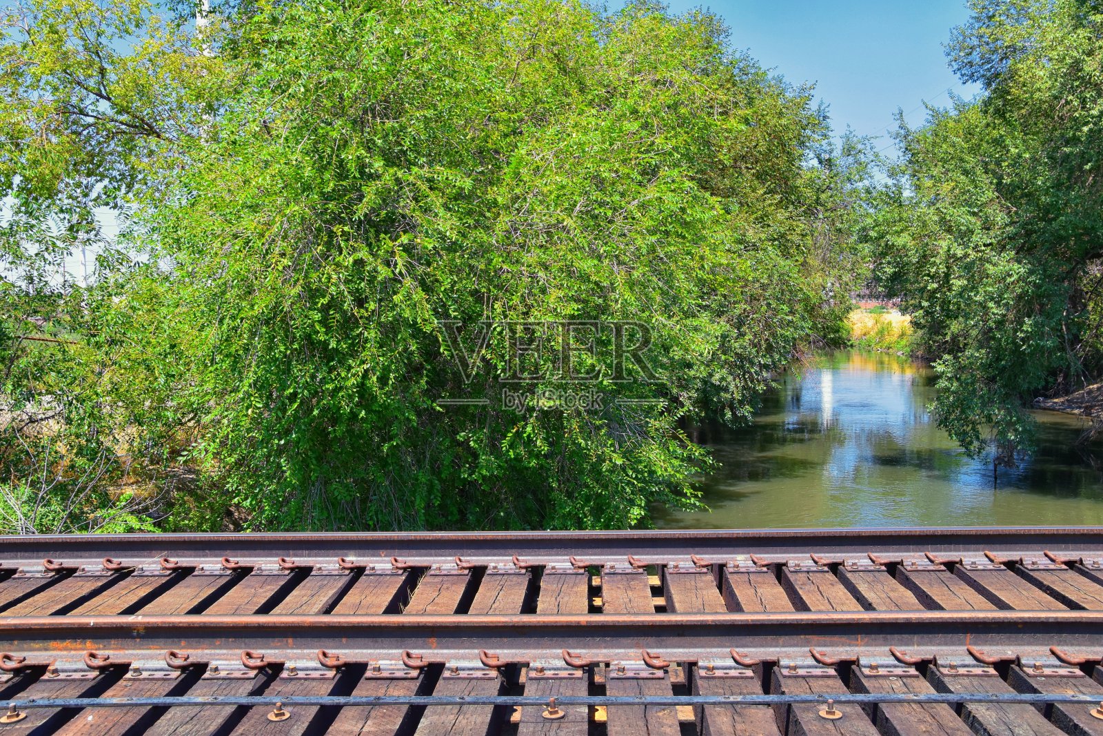 在犹他州盐湖城，约旦河步行街和火车轨道桥与周围的树木，俄罗斯橄榄，杨木和泥泞的小溪沿着瓦萨奇前落基山脉。照片摄影图片
