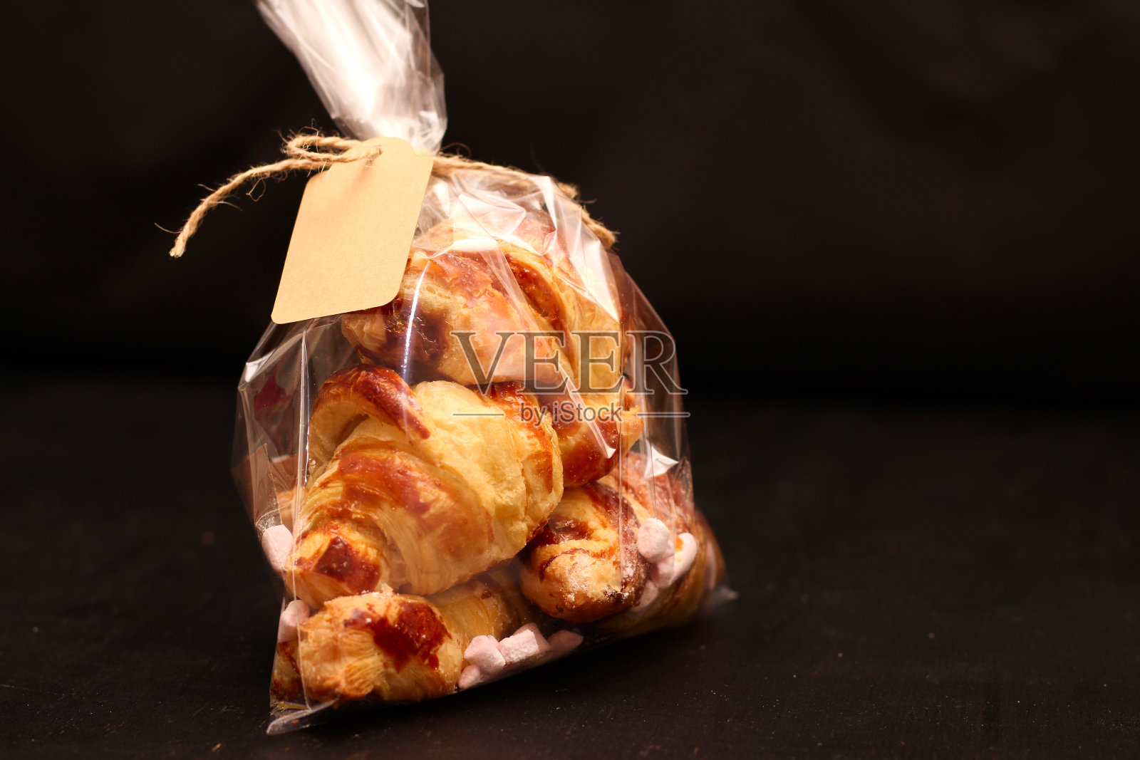 新鲜自制法式羊角面包，装在透明玻璃纸袋里，黑色桌子上有标签照片摄影图片