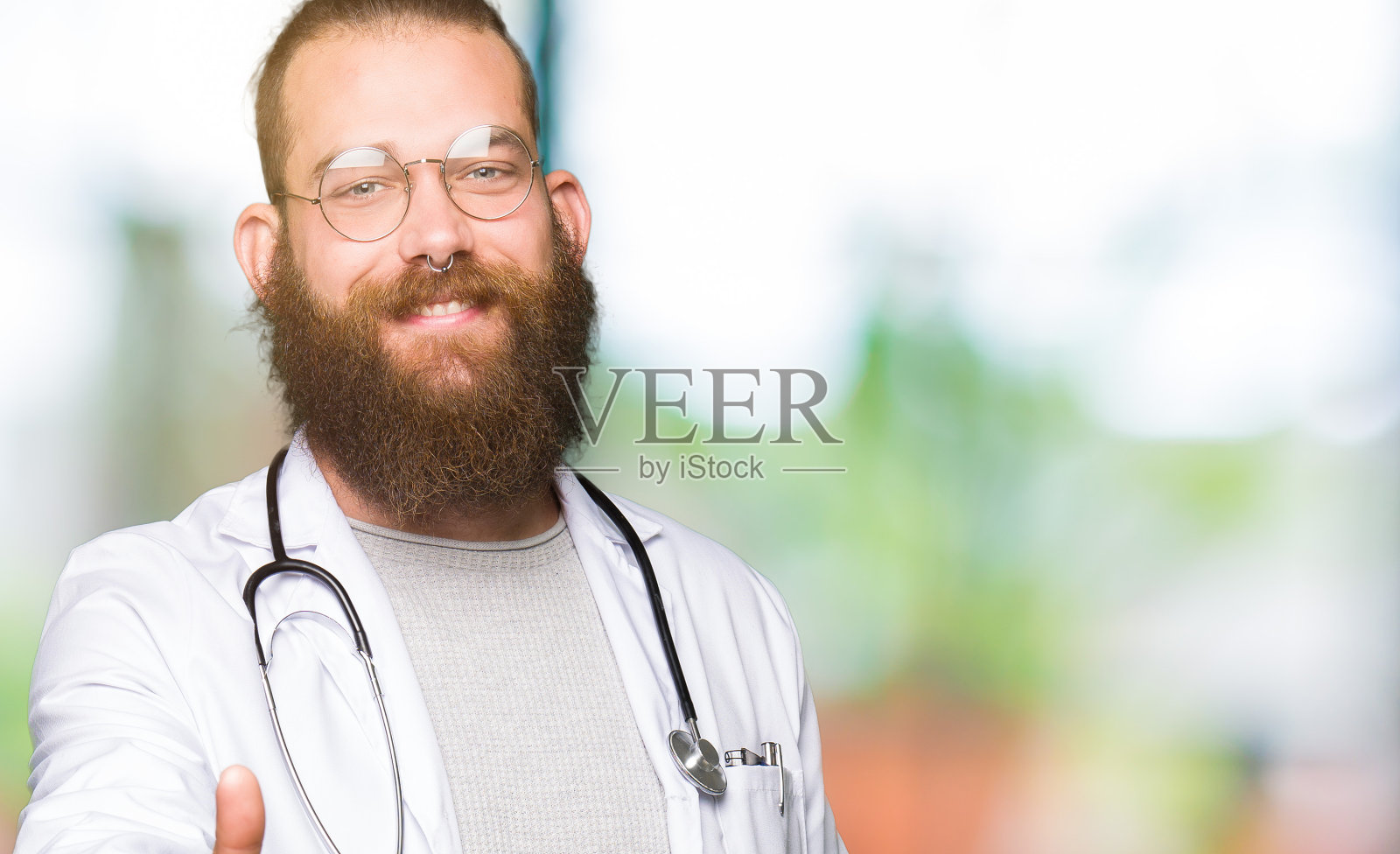 年轻的金发医生男子，胡子穿医疗大衣微笑友好地提供握手作为问候和欢迎。成功的事业。照片摄影图片