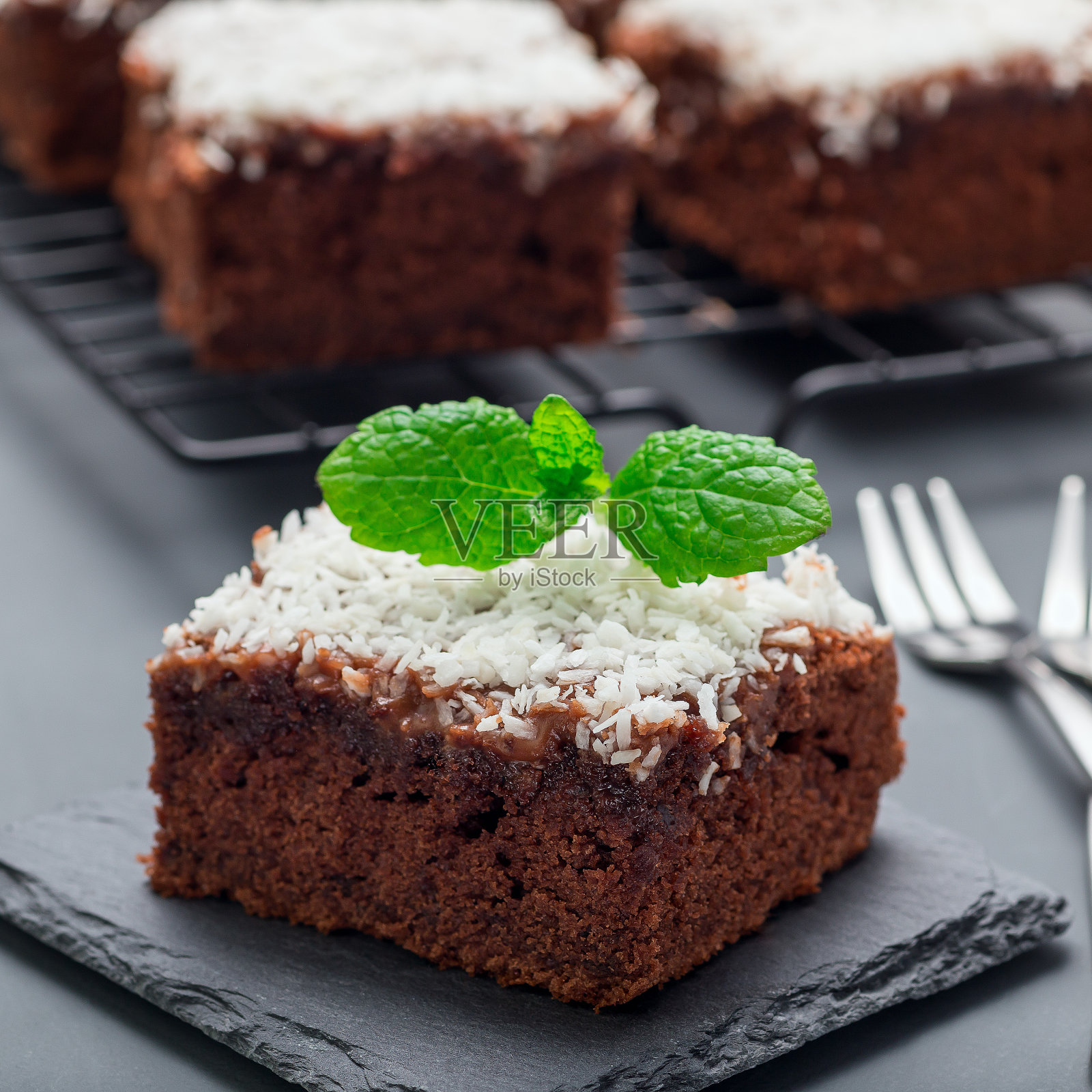 自制巧克力蛋糕配椰子片，瑞典甜品Karleksmums，切成方形，放在石盘和冷却架上，方形照片摄影图片