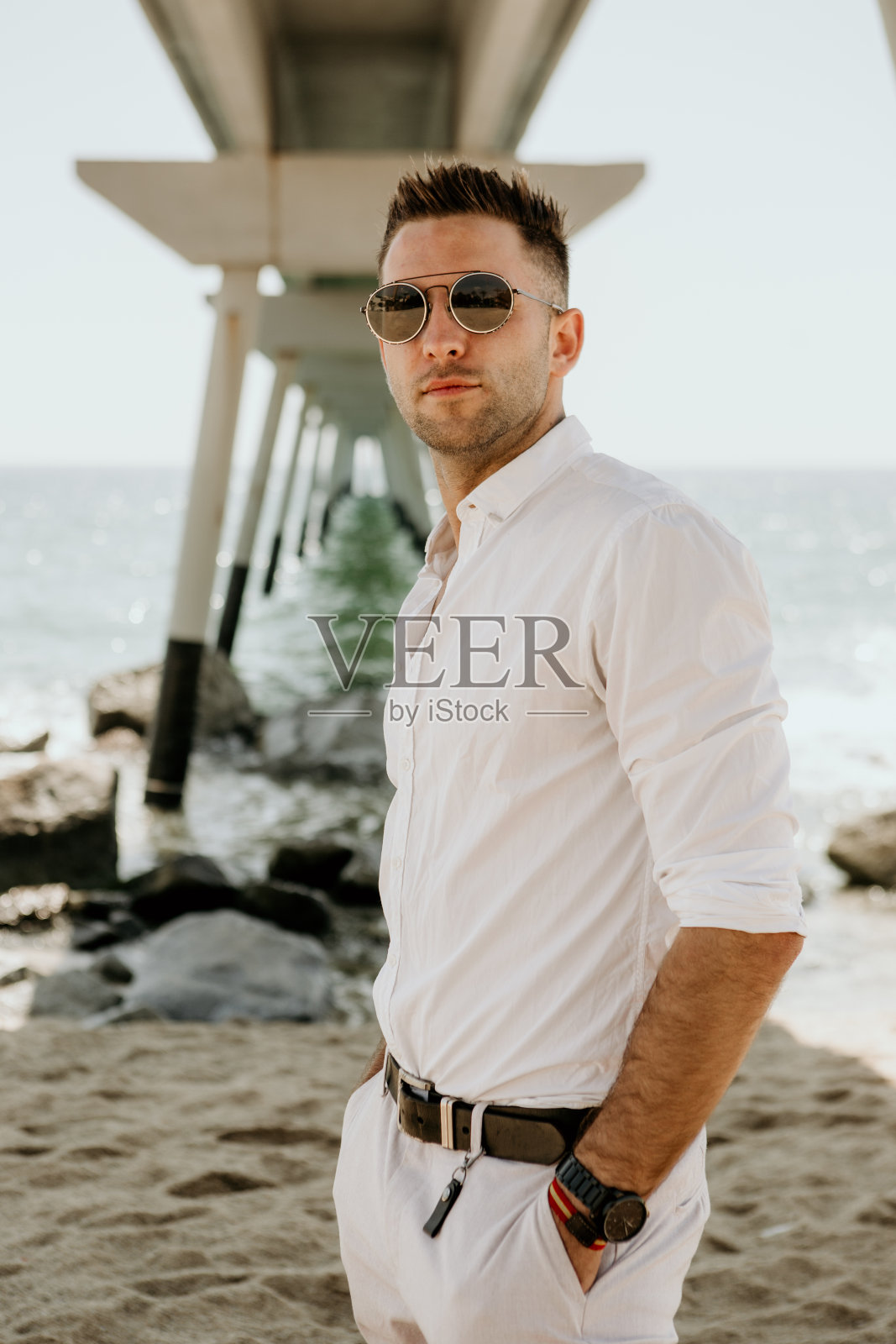 年轻英俊的男子走在海边，享受夏日。放松的白种年轻人望着阳光灿烂的日子。垂直的。照片摄影图片