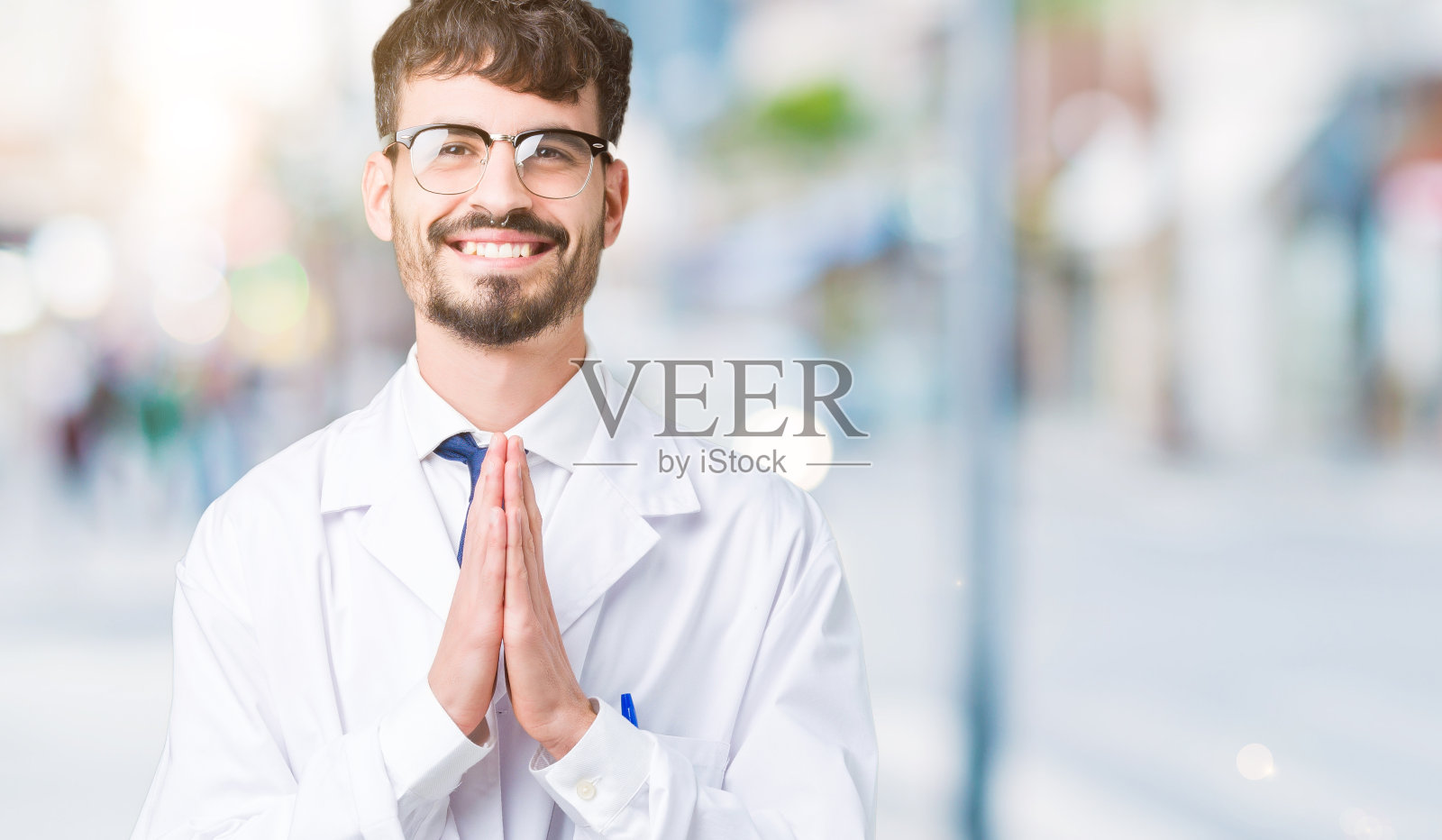 年轻的专业科学家穿着白大褂在孤立的背景下双手祈祷，自信地微笑着请求原谅。照片摄影图片