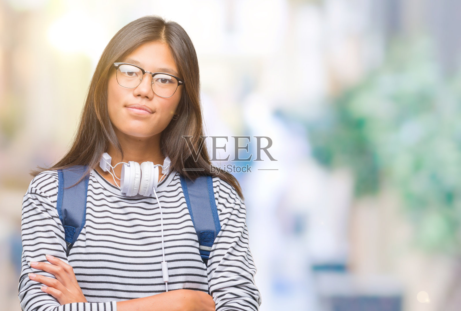年轻的亚洲女学生戴着耳机和背包在孤立的背景快乐的脸微笑，双臂交叉看着相机。积极的人。照片摄影图片