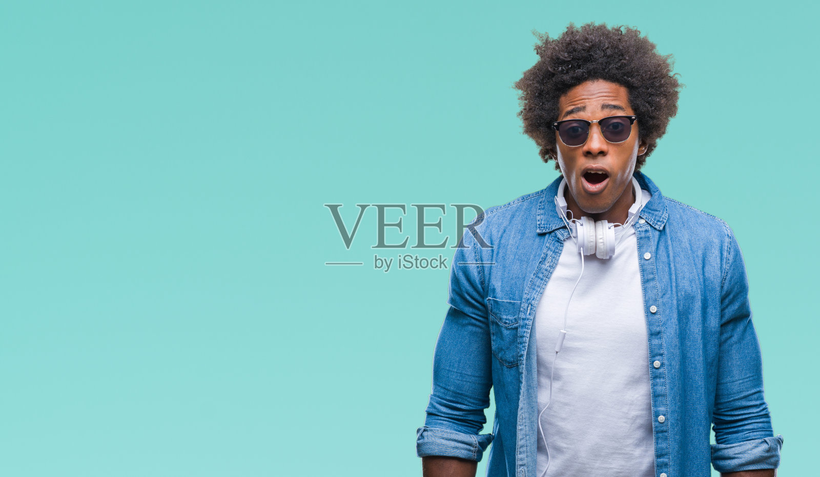 美国黑人男子戴着耳机在孤立的背景下听音乐，害怕和震惊的表情，恐惧和兴奋的脸。照片摄影图片