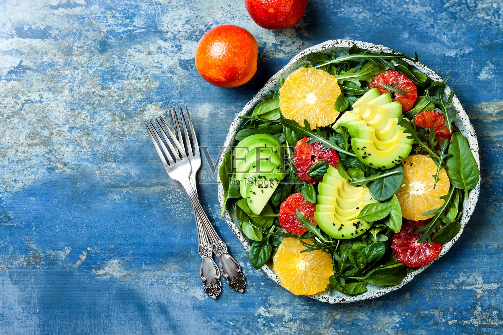 混合绿色蔬菜和血橙的柑橘沙拉。纯素、素食、清洁饮食、节食、饮食观念。蓝石头背景。照片摄影图片
